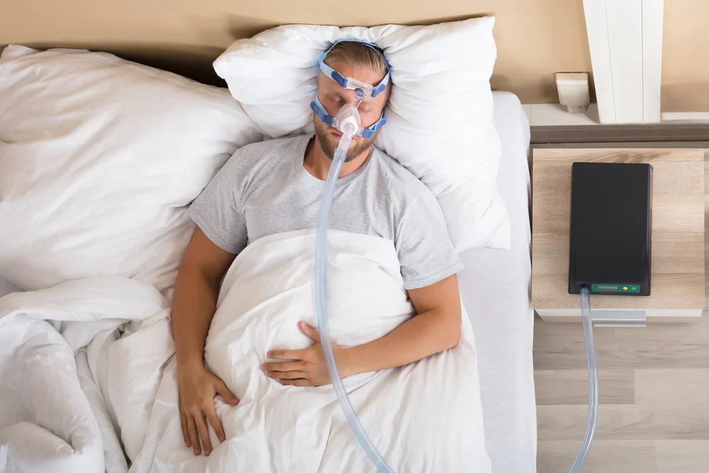 Homem dormindo de forma confortável utilizando máscara e aparelho CPAP para tratar apneia do sono.
